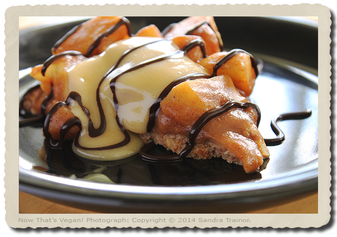 A vegan and gluten-free apple pie with a nut crust, vanilla cream, and chocolate sauce.